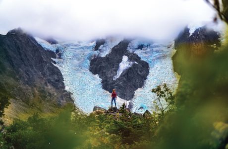 Woman hiking through rugged landscape in Alaska through misty clouds to ice and rock formations.