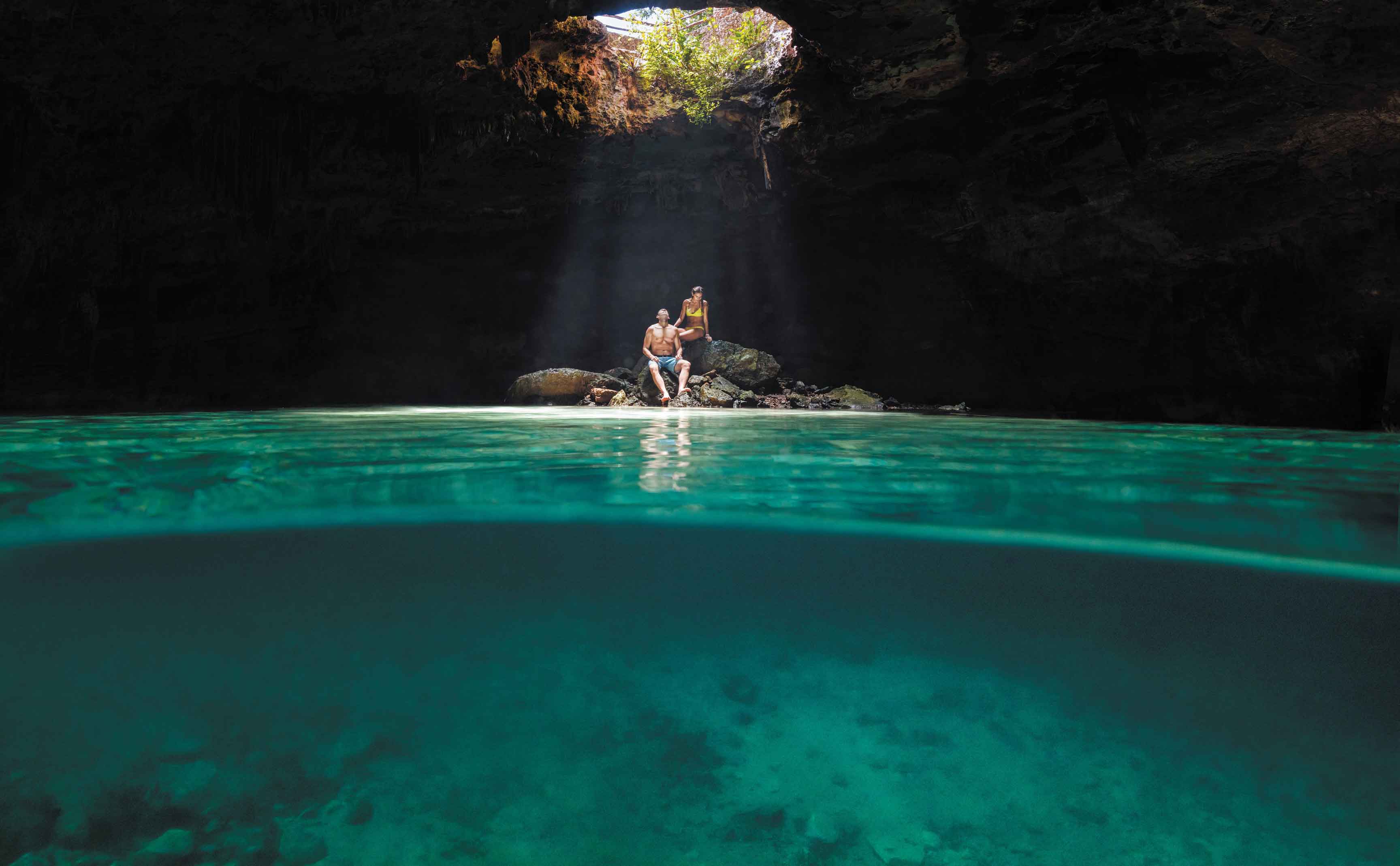 Verliebtes Paar sitzt während ihrer Kreuzfahrt in einer Cenote bzw. Unterwasserhöhle auf Steinen in Cozumel, Mexiko 