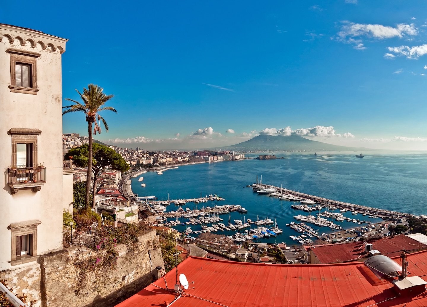 Naples’ port stretches toward Posillipo Hill, with Mount Vesuvius rising beyond the Mediterranean shoreline. - Naples, Italy