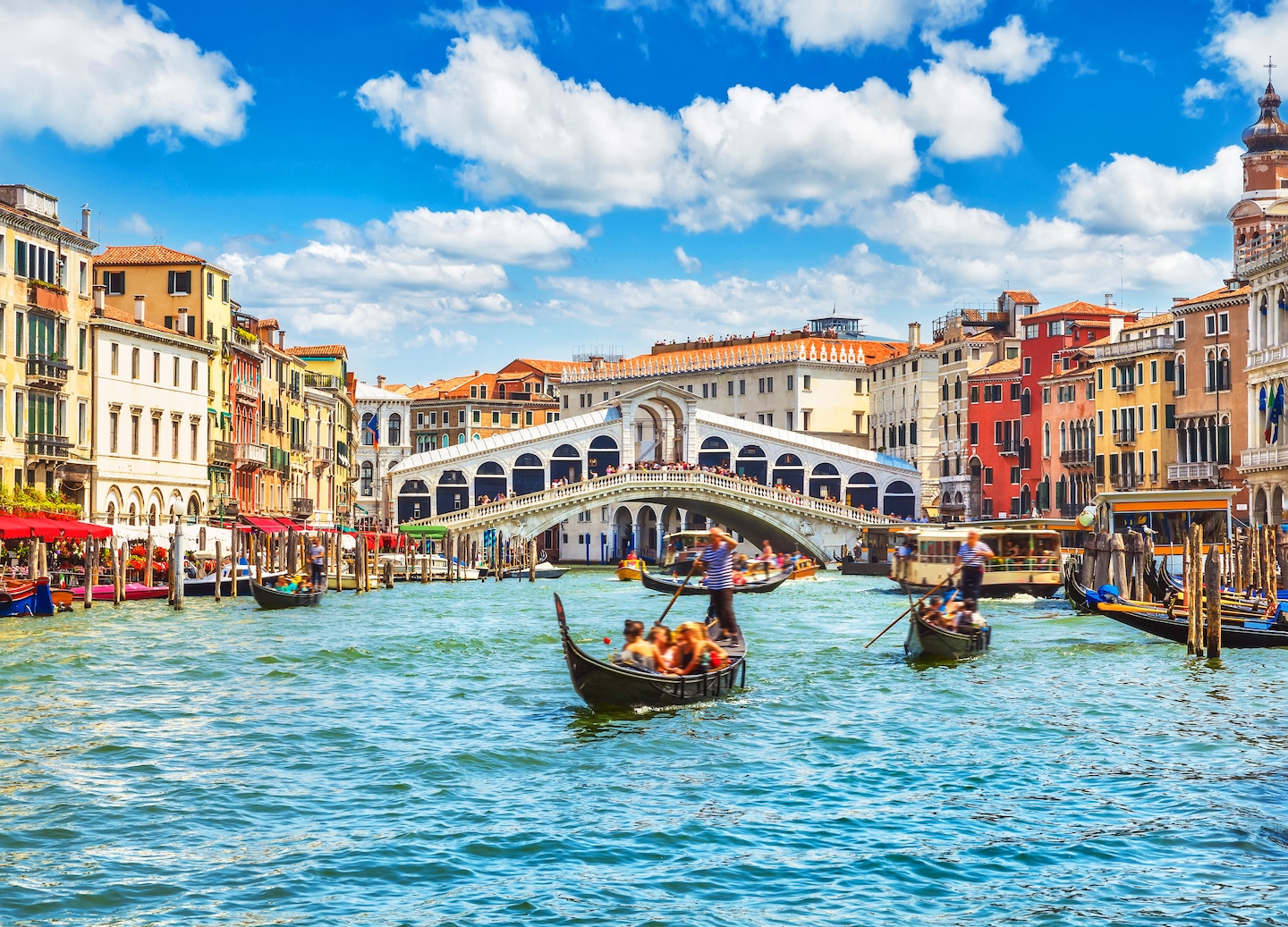 The Rialto Bridge arches over Venice’s Grand Canal beneath bright sky and soft clouds. - Venice, Italy