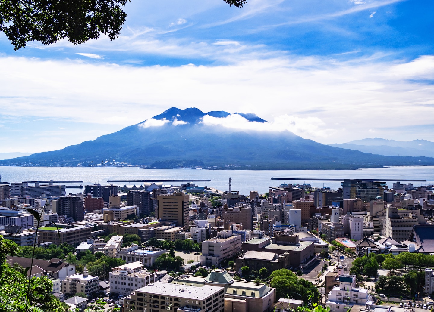 Mt. Sakurajima towers over Kagoshima City, seen from Shiroyama Observatory beneath a soft, hazy sky. - Kagoshima, Japan