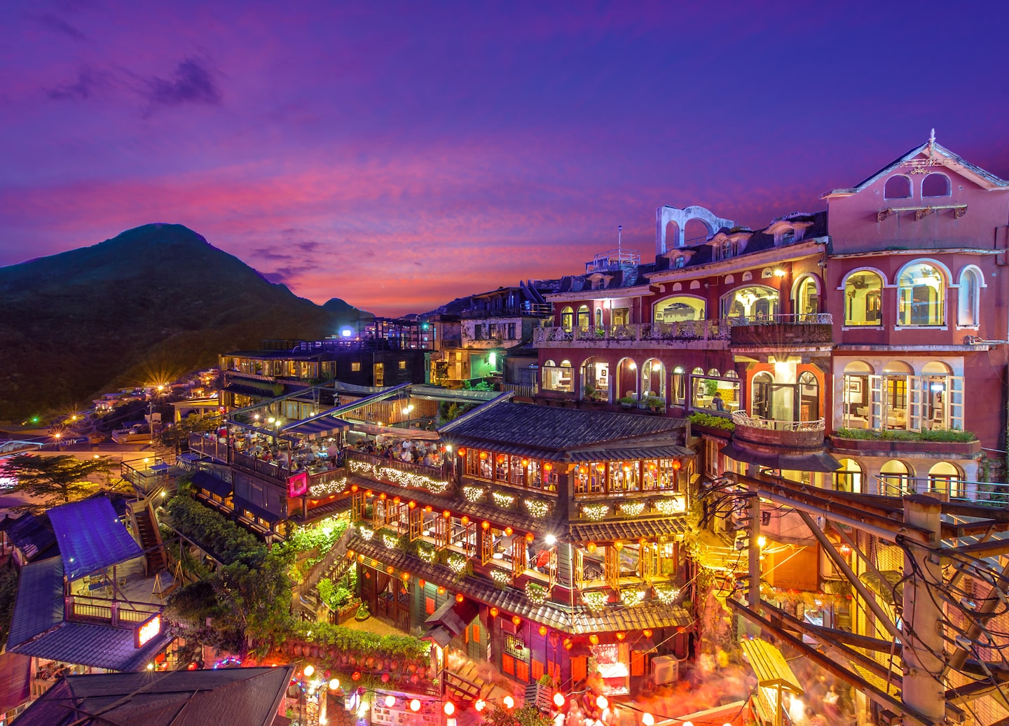 Jiufen’s hillside teahouses glow with red lanterns, lighting the narrow streets at night. - Taipei