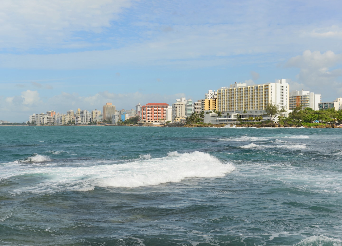 Beachfront towers overlook bright turquoise water and sunlit shoreline. - Puerto Rico