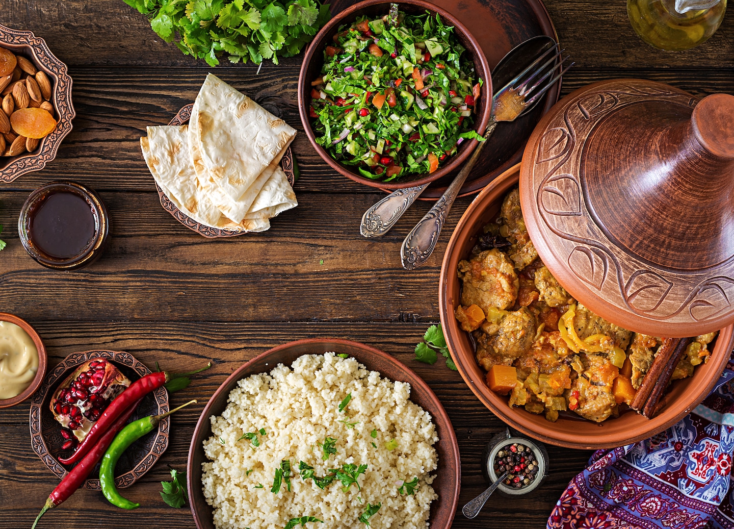 A lamb tagine, couscous, and fresh salad sit arranged on a rustic wooden table. - Morocco 