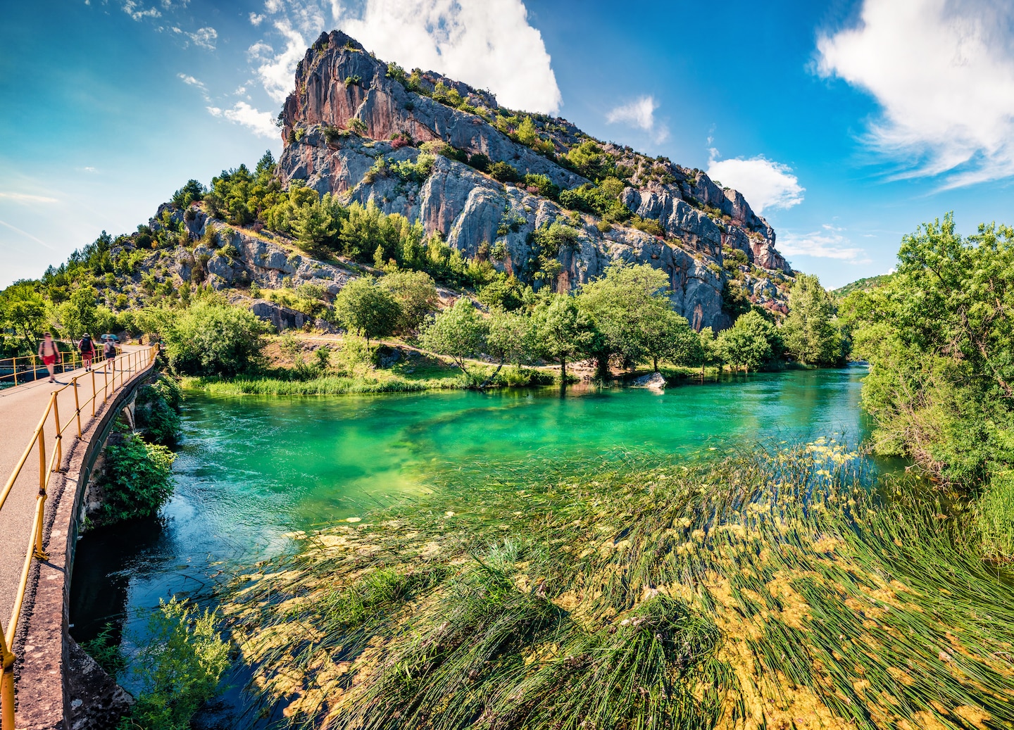 Visitors walking over a bridge towards the lush forest in Krka National Park. - Split, Croatia