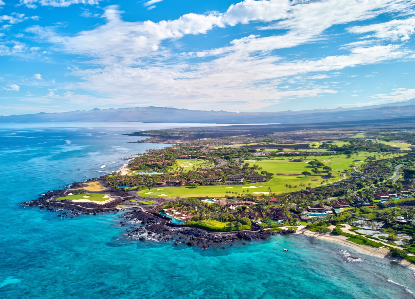 South Kohala’s coastline shows turquoise water, rugged lava rock, and bright green slopes under clear sky. - Kailua-Kona, Hawaii