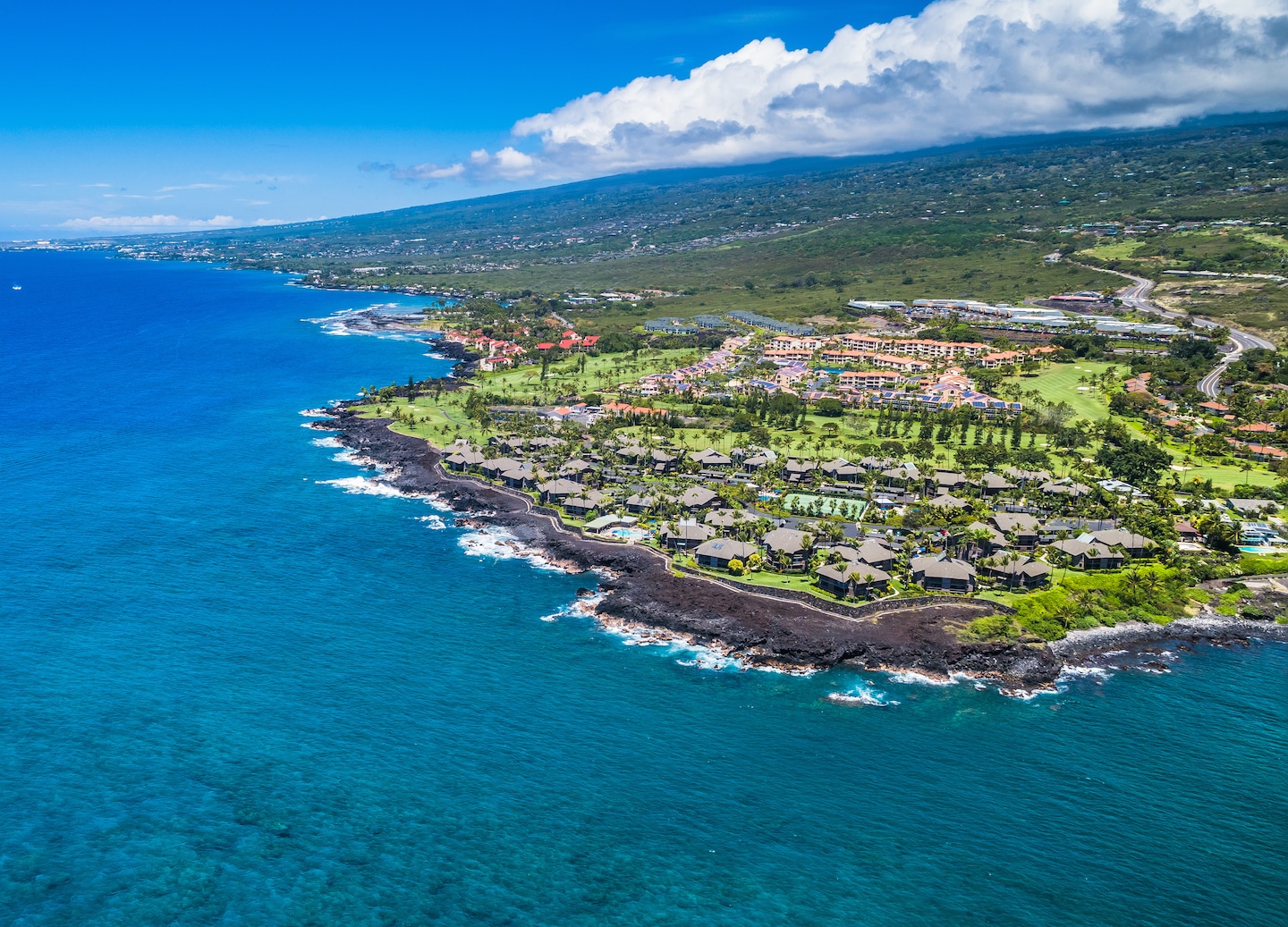 An aerial view of Kailua‑Kona shows blue coastline, green hills, and clustered seaside buildings. - Kailua‑Kona, Hawaii