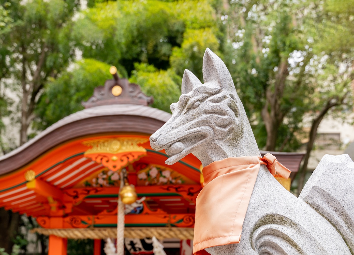 A stone kitsune statue stands at Ikuta Shrine, framed by red pillars. - Kobe, Japan
