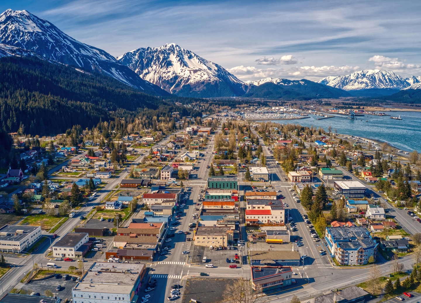 Seward’s shoreline meets bright blue water, backed by forested hills and distant snow‑capped peaks. - Seward, Alaska