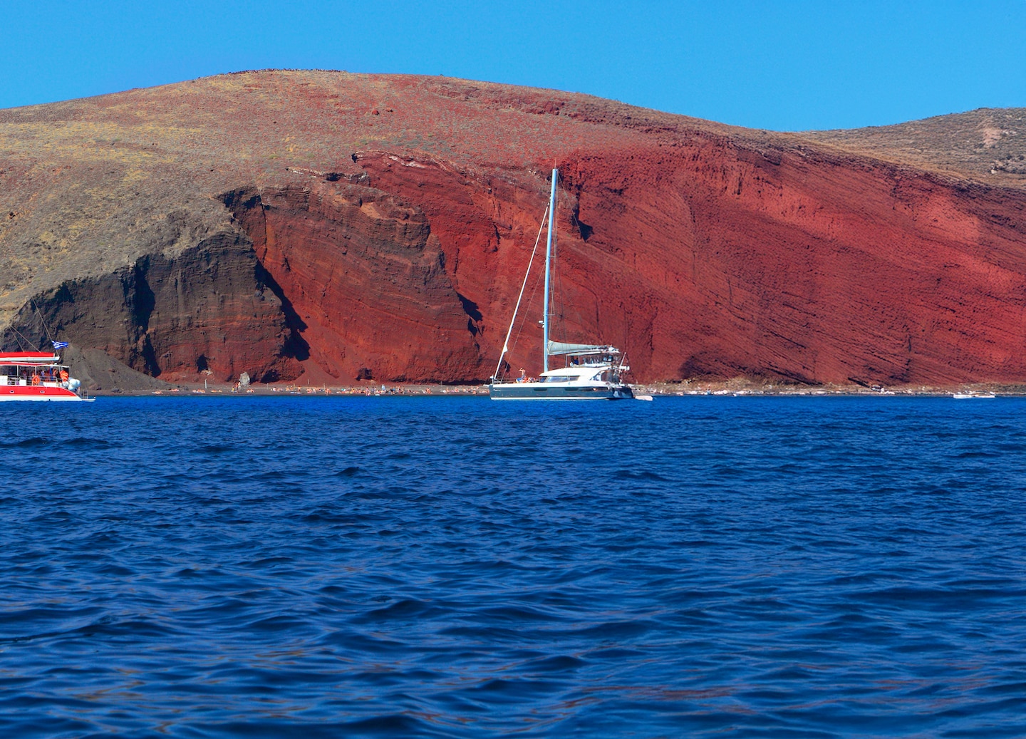 Red Beach’s towering cliffs frame turquoise water under Santorini’s bright sun. - Santorini, Greece
