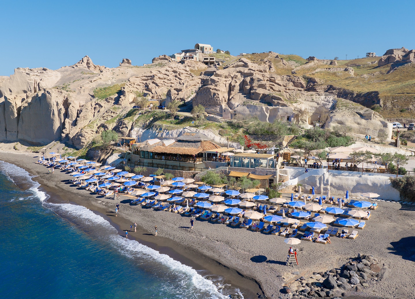 White‑roofed cabanas and terraces line the coast at the Royal Beach Club Santorini. - Santorini, Greece
