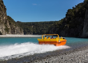 jetboat in clear blue water surrounded by mountains in new zealand