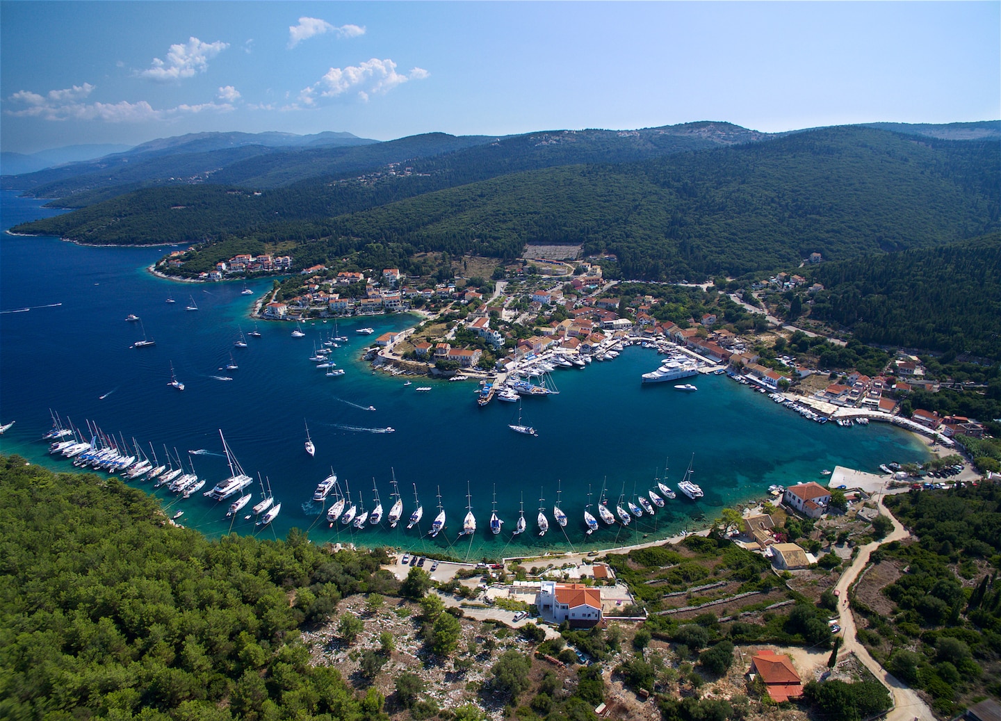 Aerial view of Fiskardo village by coastal cliffs and blue sea. - Cephalonia
