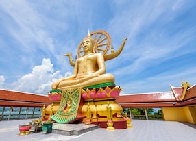 large gold buddha statue in a sitting position under the blue sky at big buddha temple is a famous