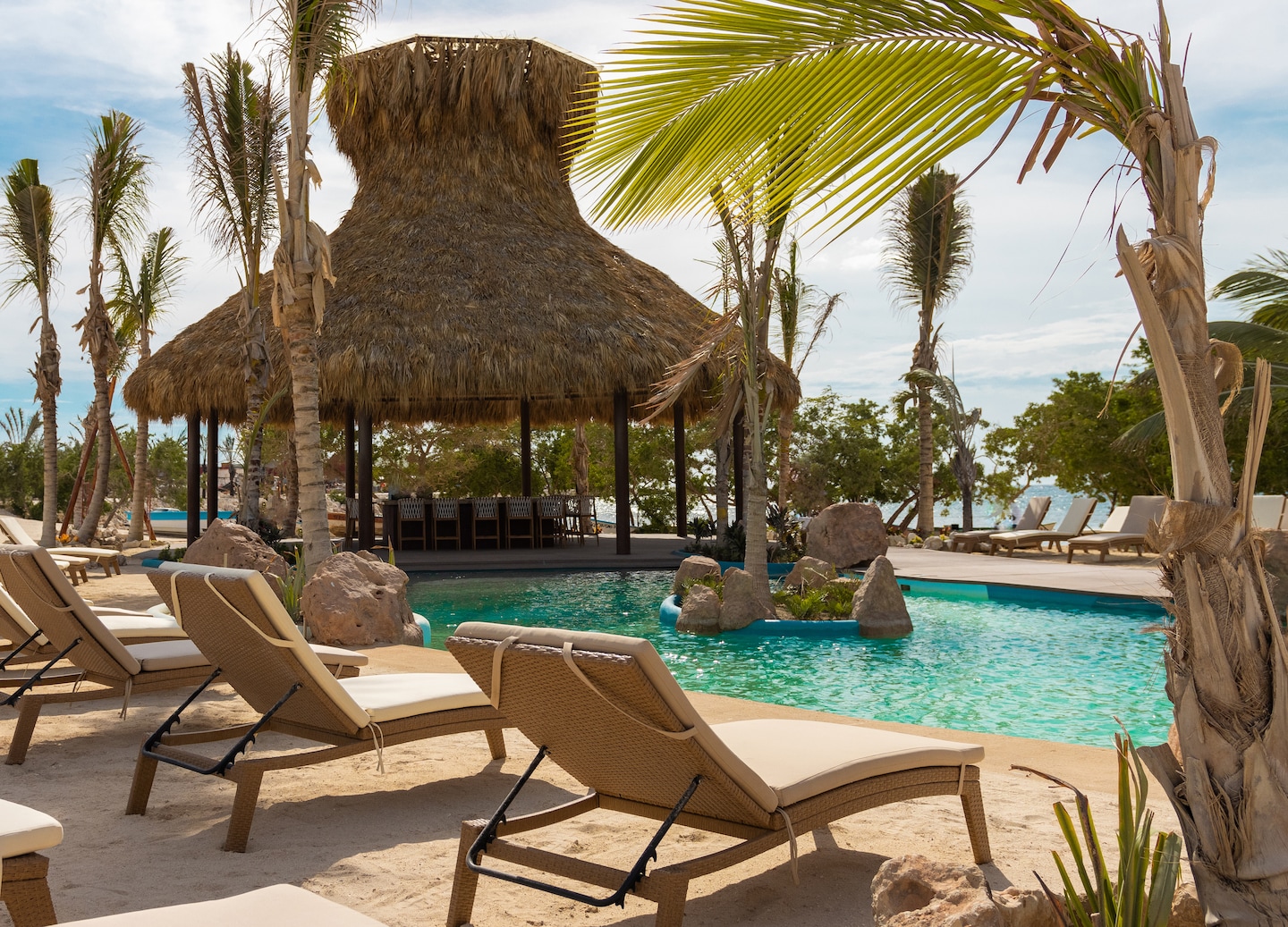 Poolside loungers overlook calm turquoise water, with palm trees framing a relaxed beach setting. - Cabo Rojo, Dominican Republic