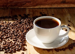 coffee in white cup and coffee beans on older wood background with ligh from windows