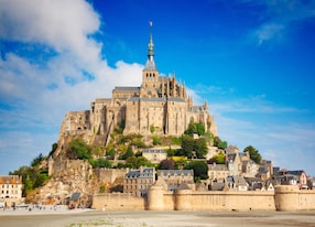 view of famous historic le mont saint michel tidal island on a sunny day with blue sky and clouds