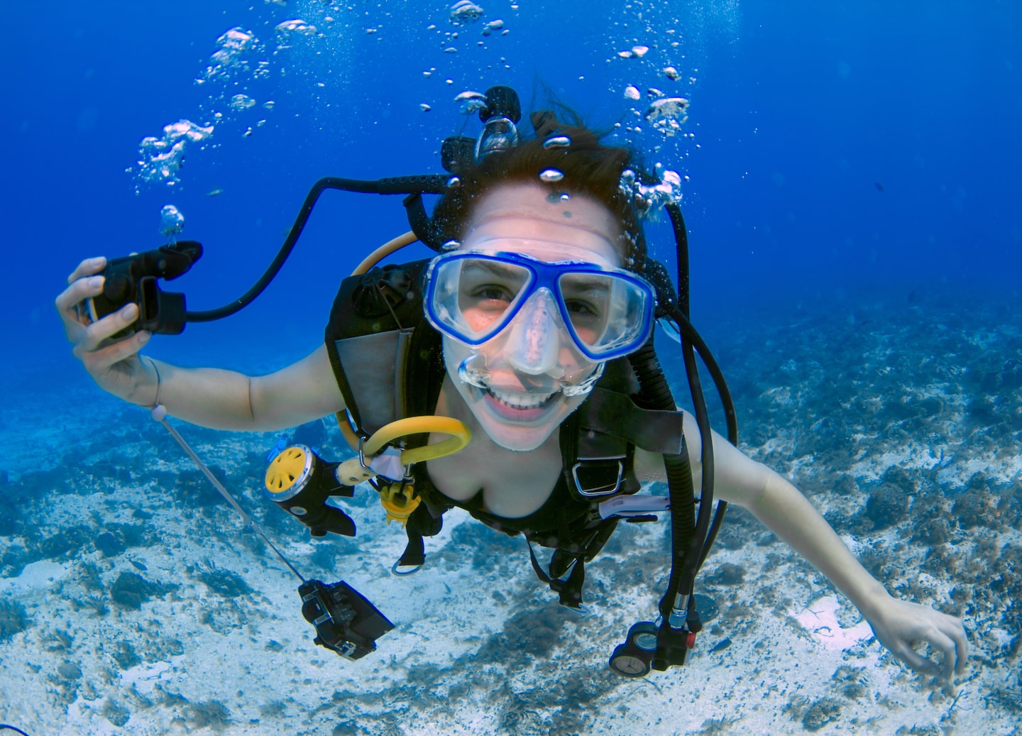 A smiling scuba diver poses underwater, holding her regulator while wearing a bright blue mask. - CocoCay, Bahamas 