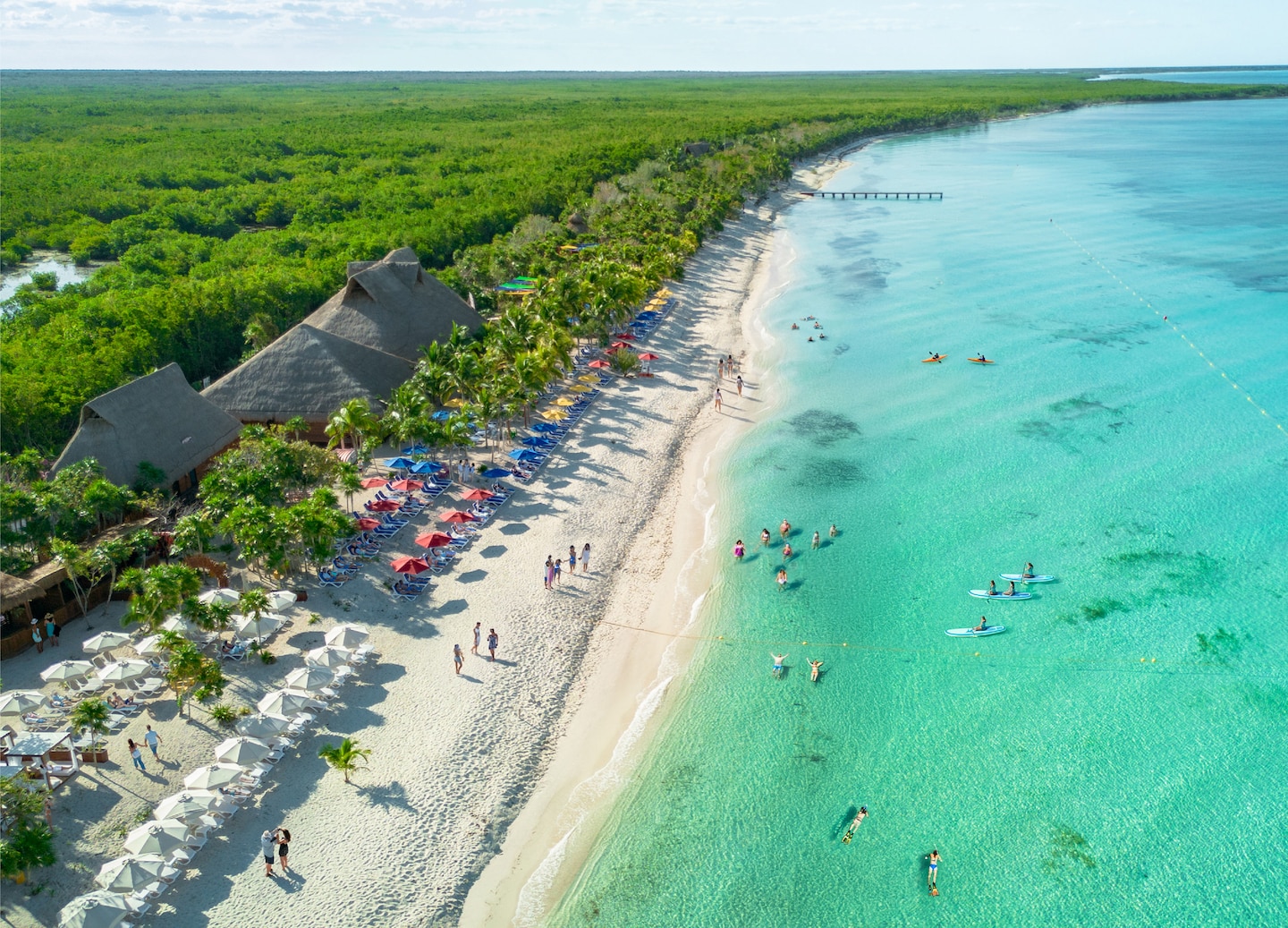 An aerial view shows KUZA Beach Park’s bright turquoise water, white sand, and palm-lined shoreline. - Cozumel, Mexico