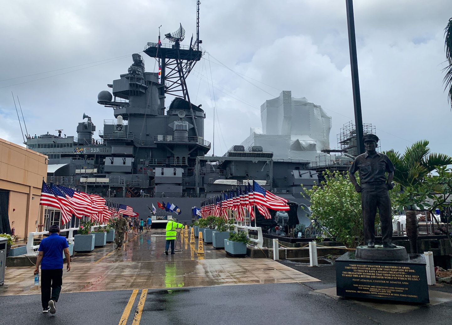 Visitors walk toward the Pearl Harbor Visitor Center, surrounded by palm trees and waterfront views. - Honolulu, Hawaii