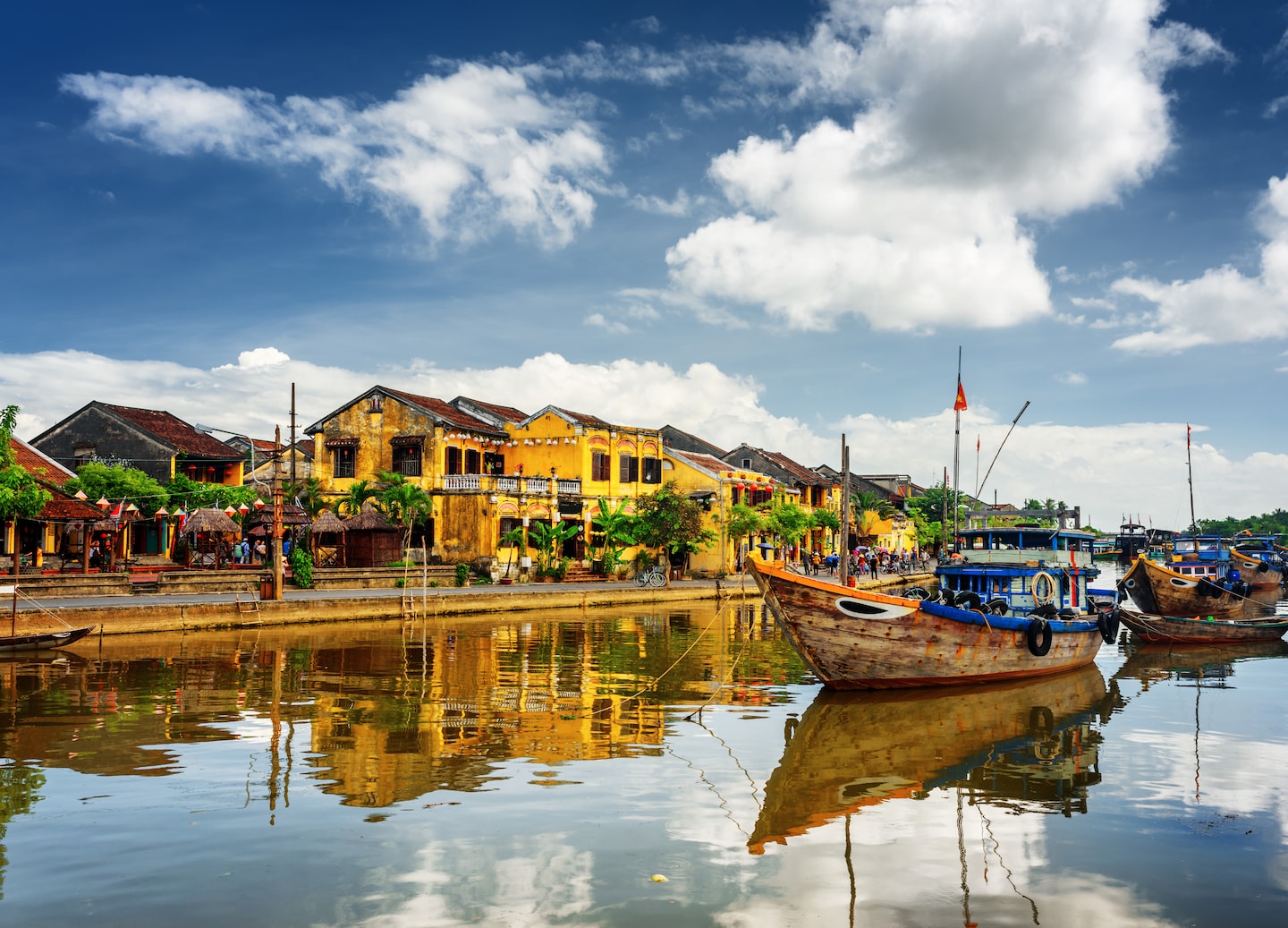 Wooden boats rest along a calm Vietnamese river in Hoi An, with lantern‑lit buildings reflecting on the water. - Vietnam