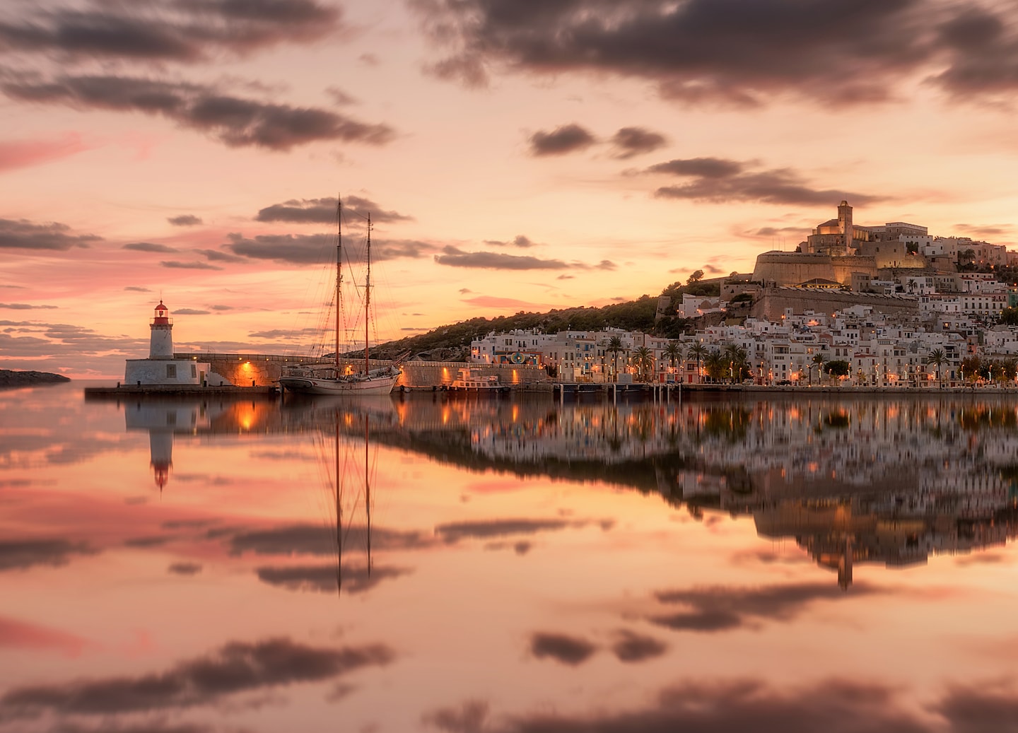 D’Alt Vila overlooks the harbor as sunset colors reflect across the calm water. - Ibiza, Spain