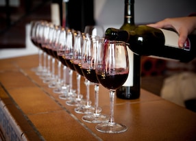 woman hand with wine bottle pouring a row of glasses for tasting