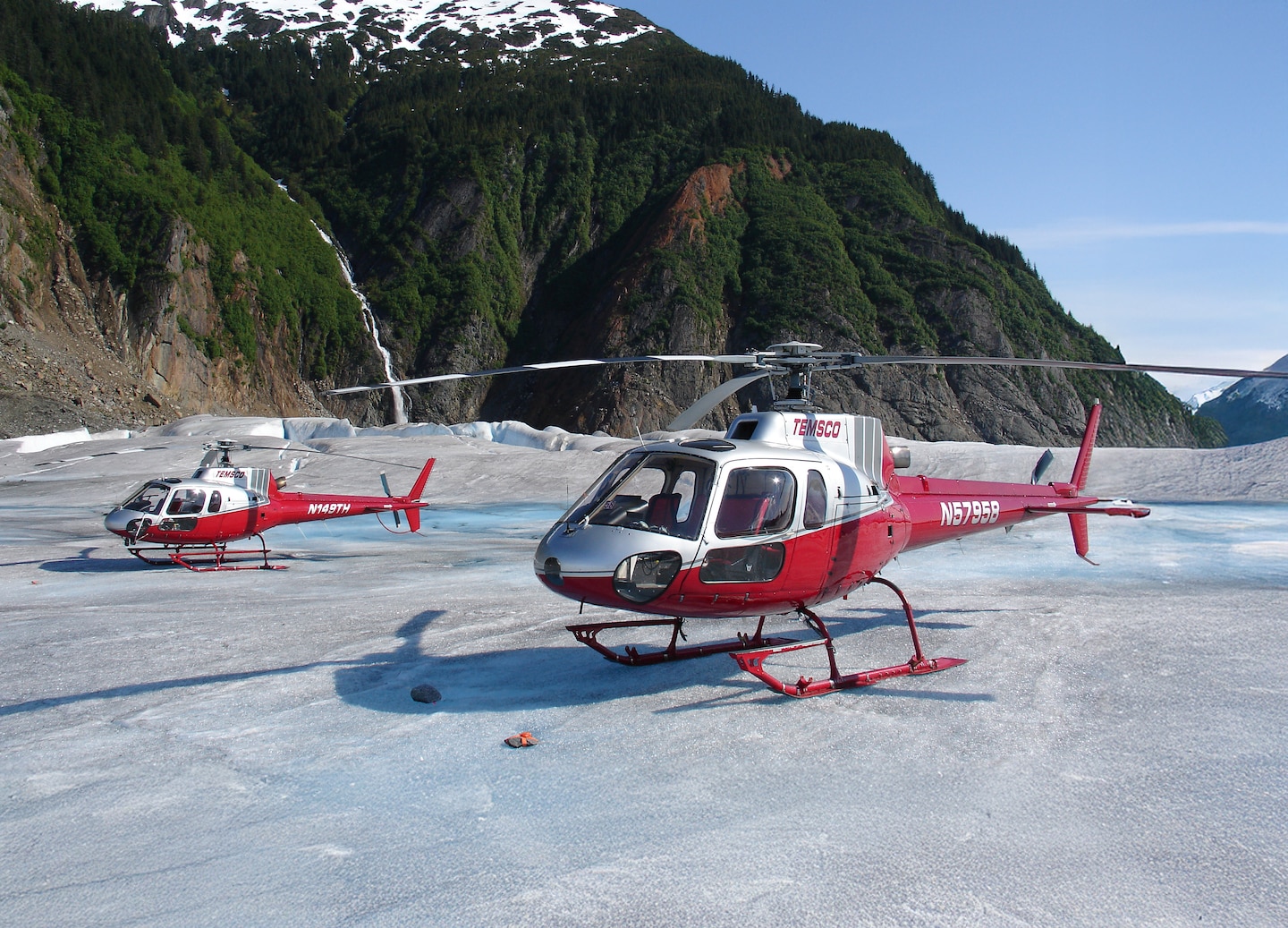 Parked helicopters rest on glacial ice beneath towering Mendenhall peaks. - Juneau, Alaska