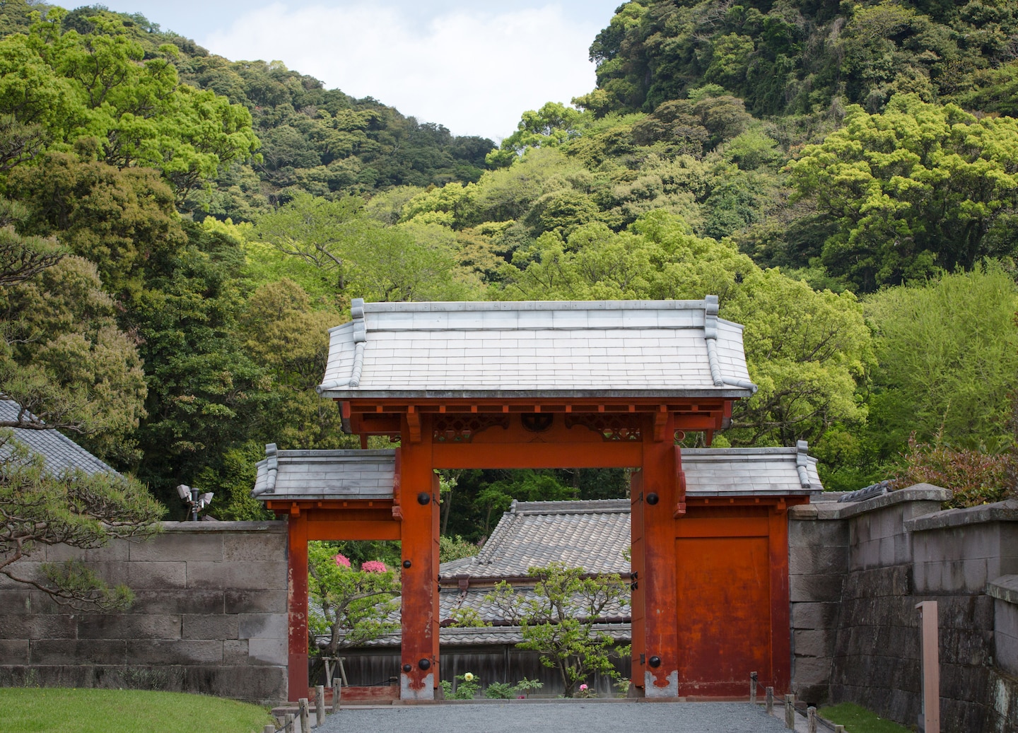 A red‑lacquered pagoda gate stands amid lush greenery at Kagoshima’s historic Sengan‑en Garden. - Kagoshima, Japan