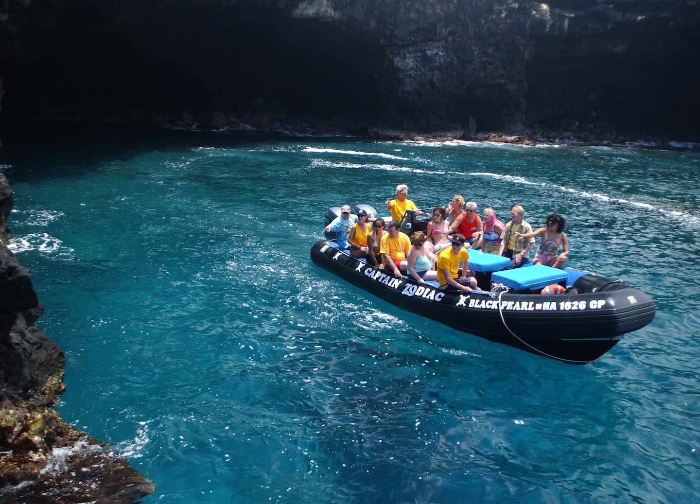 A Zodiac raft approaches sea caves, where dark volcanic rock meets bright turquoise Hawaiian water. - Kailua-Kona, Hawaii