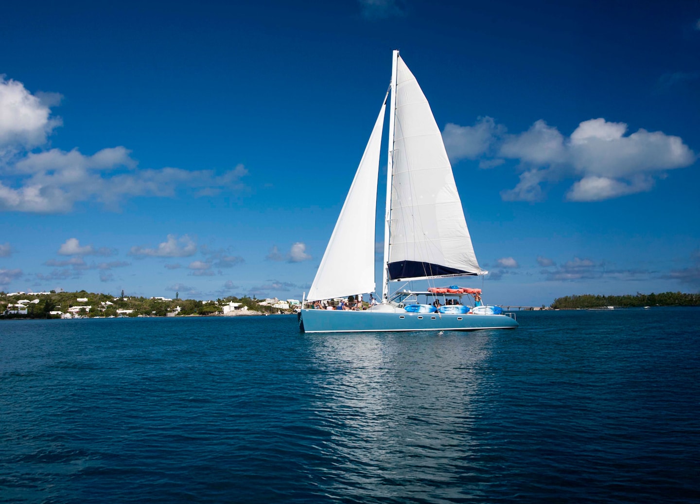 A catamaran glides across Bermuda’s bright turquoise water as guests relax on deck in the sun. - Royal Naval Dockyard, Bermuda