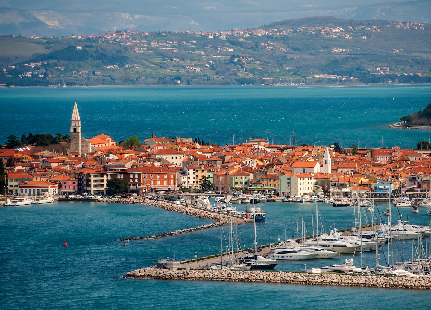 Izola’s pastel waterfront homes rise above a calm Adriatic harbor lined with small boats. - Izola, Slovenia