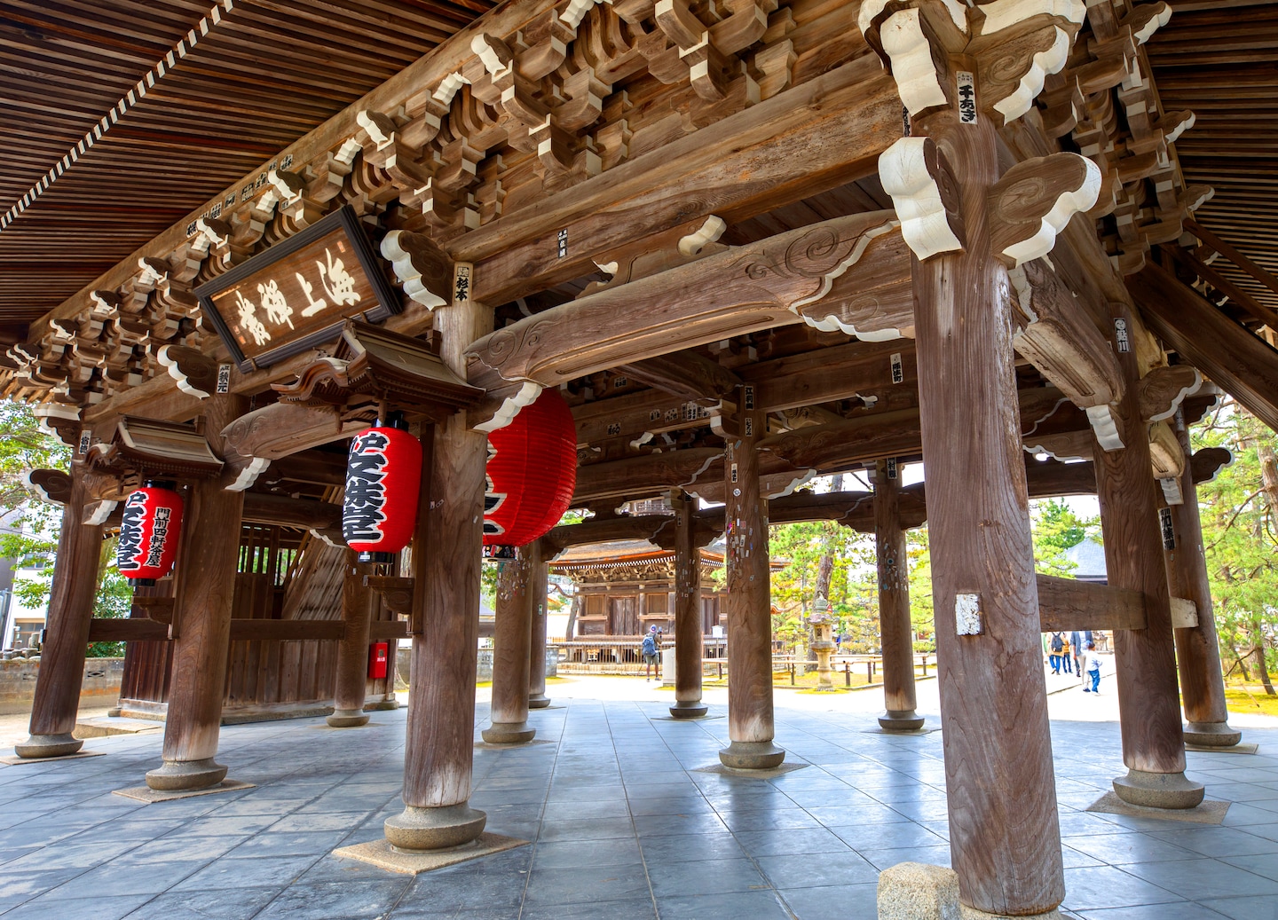 A traditional temple building stands among tall trees, with carved wooden details framing its entrance. - Kyoto (Maizuru), Japan