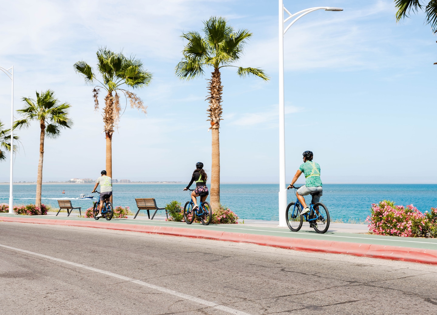 Cyclists ride along the sunny La Paz boardwalk with ocean views and palm‑lined pathways. - La Paz, Mexico