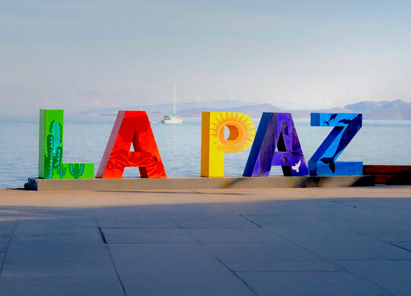 Colorful La Paz sign stands along the waterfront with blue sea and mountains behind it. - La Paz, Mexico