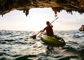 young lady paddling the kayak in a sea near the cave exit