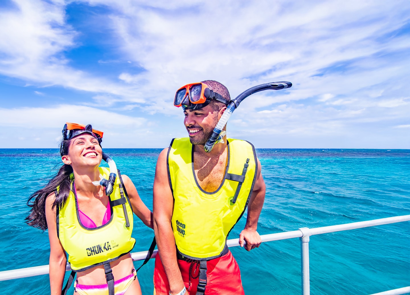 A couple relaxes on a catamaran, smiling as they sail over calm turquoise Caribbean water. - Montego Bay, Jamaica