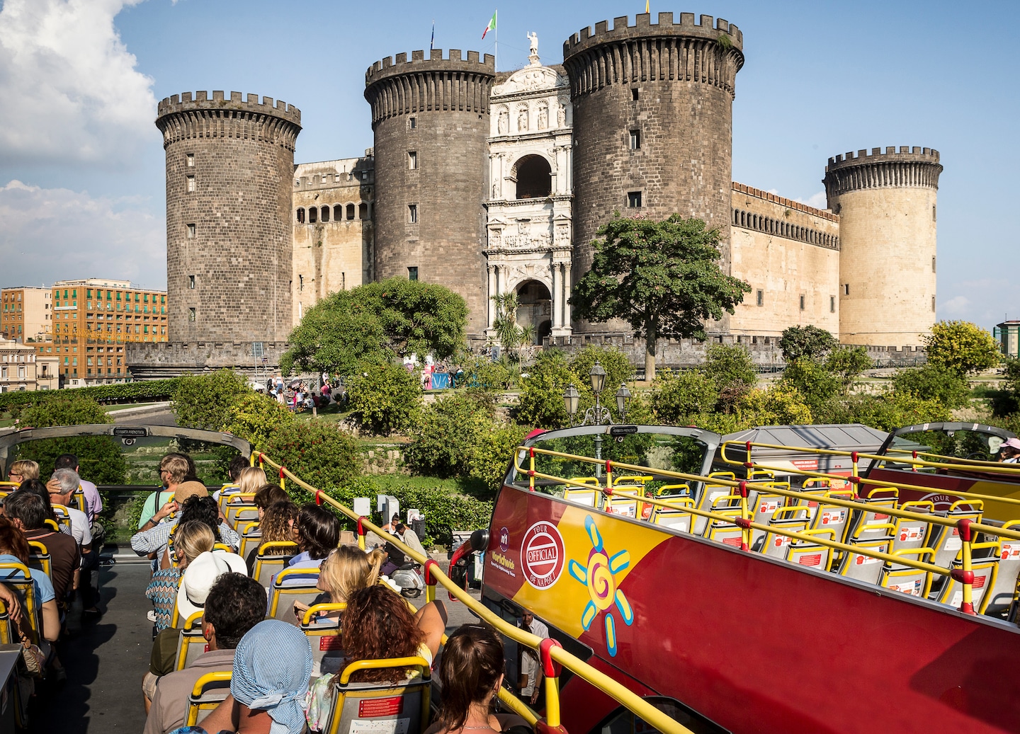 An open‑air sightseeing bus passes Naples’ medieval Maschio Angioino castle. - Naples, Italy