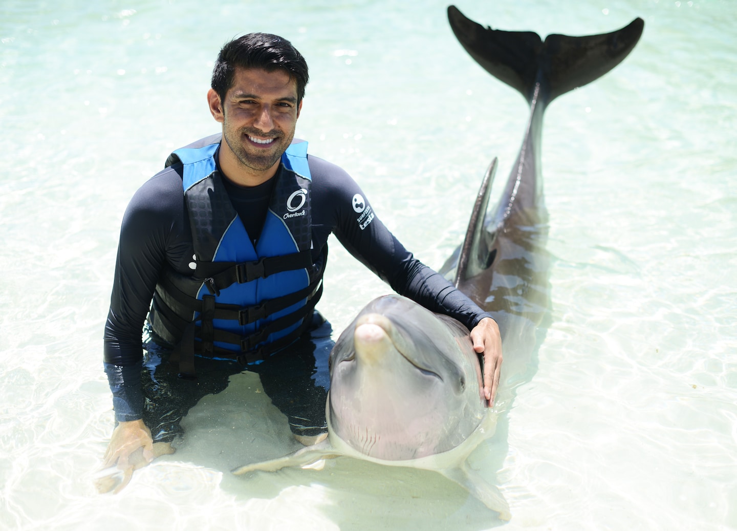 A guest gently holds a dolphin during a supervised swim, smiling in the clear lagoon water. - Nassau, Bahamas