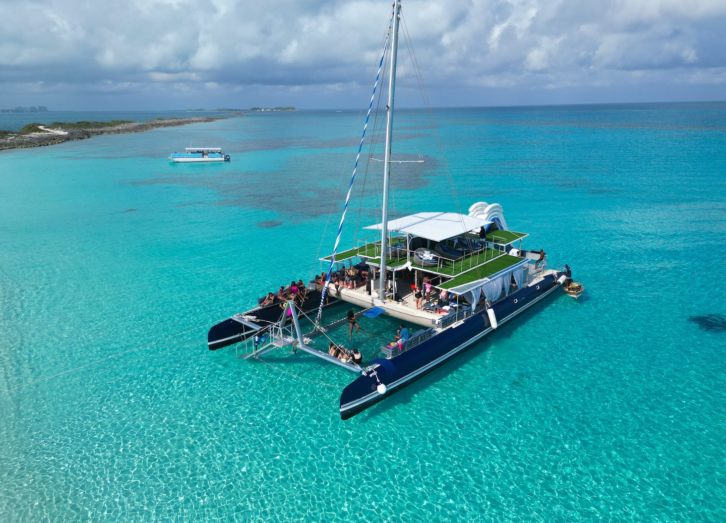 A catamaran party gathers offshore as guests relax on a sunny sandbar. - Nassau, Bahamas