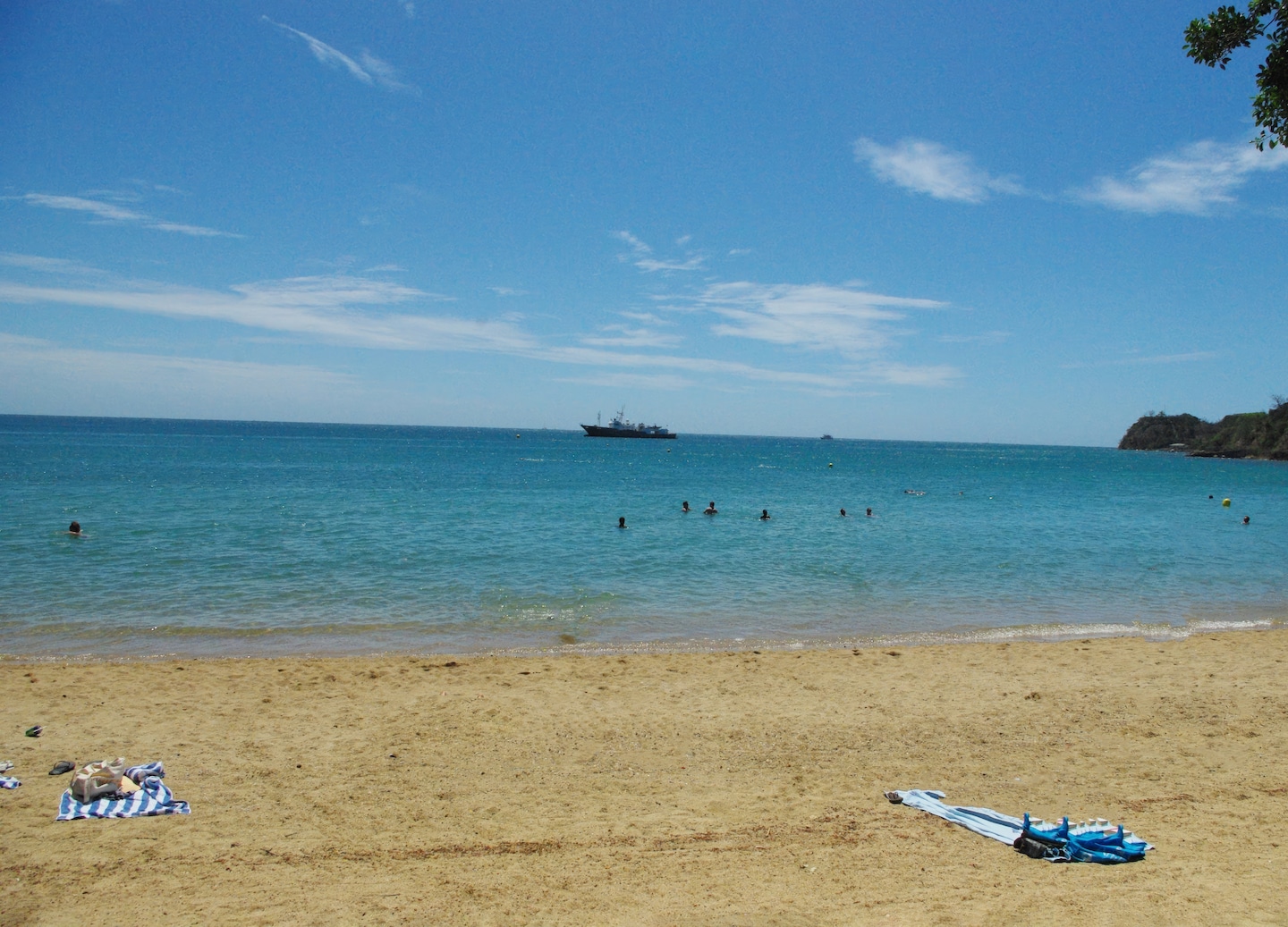 Lemon Bay’s calm turquoise water meets a sandy shoreline lined with palm trees and bright sun. - Noumea, New Caledonia