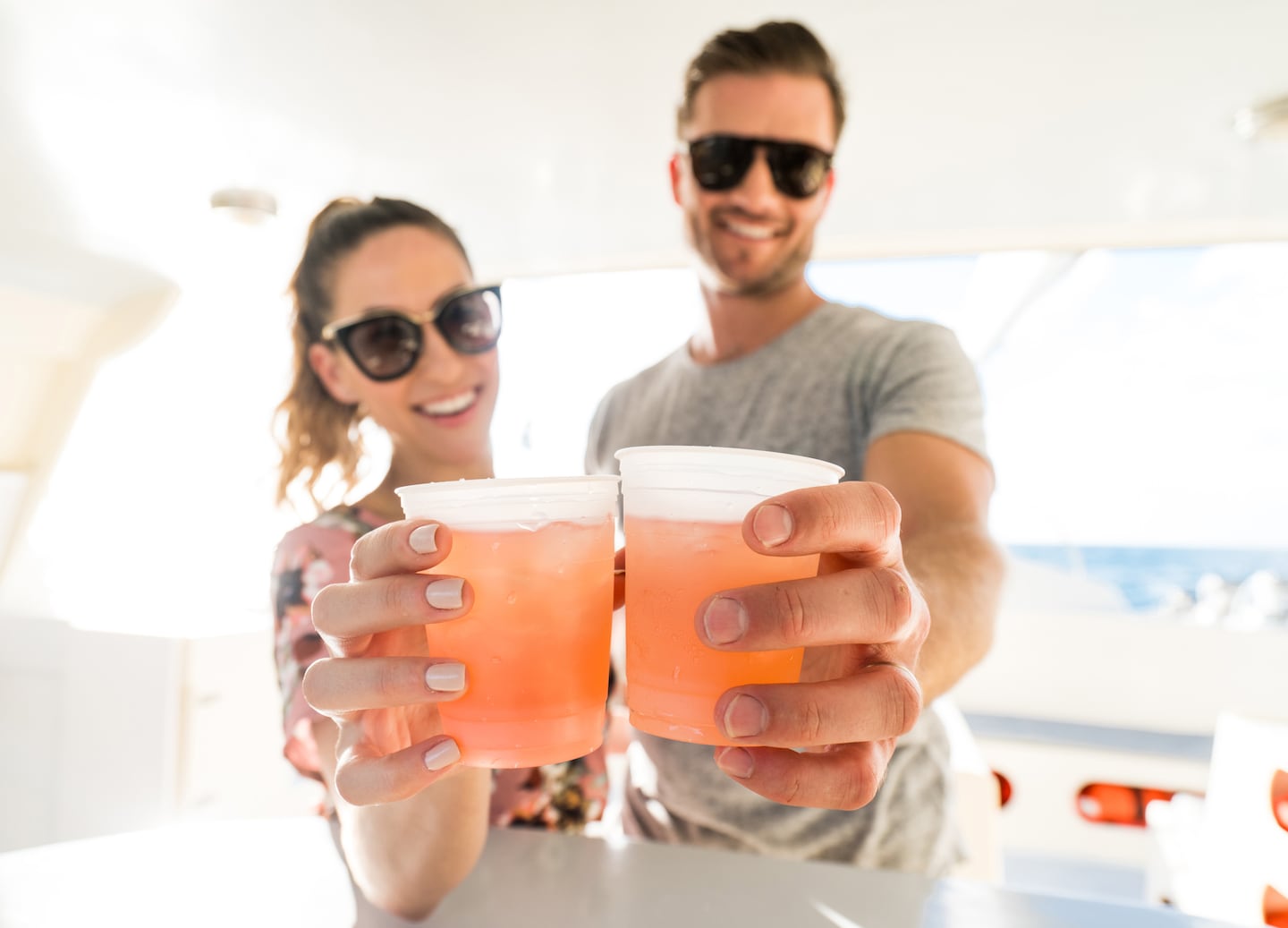 A couple wearing sunglasses toasts with drinks. - Bahamas