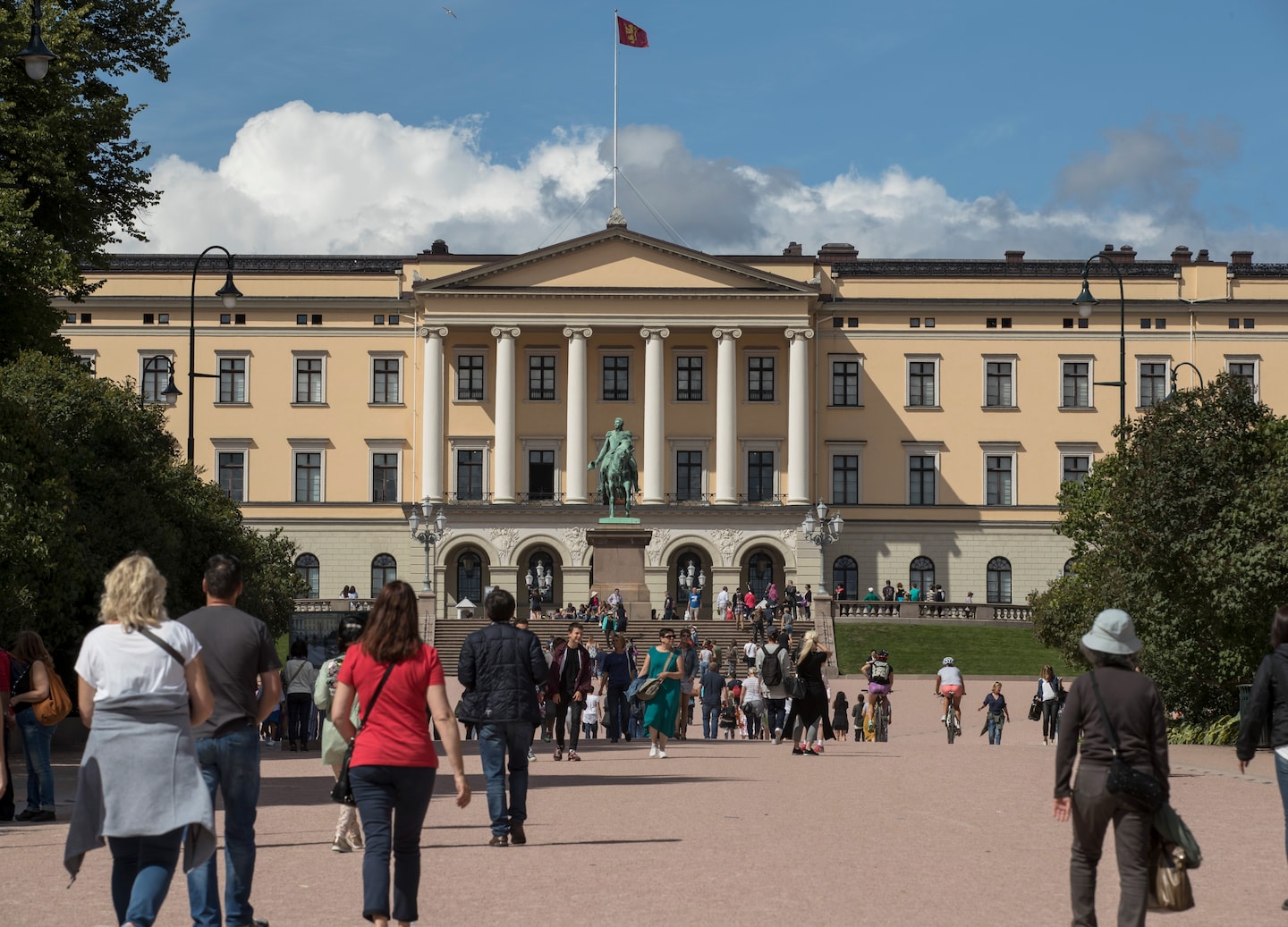 Tourists walk near the Royal Palace as sculptures stand along Oslo’s calm, tree‑lined grounds. - Oslo, Norway
