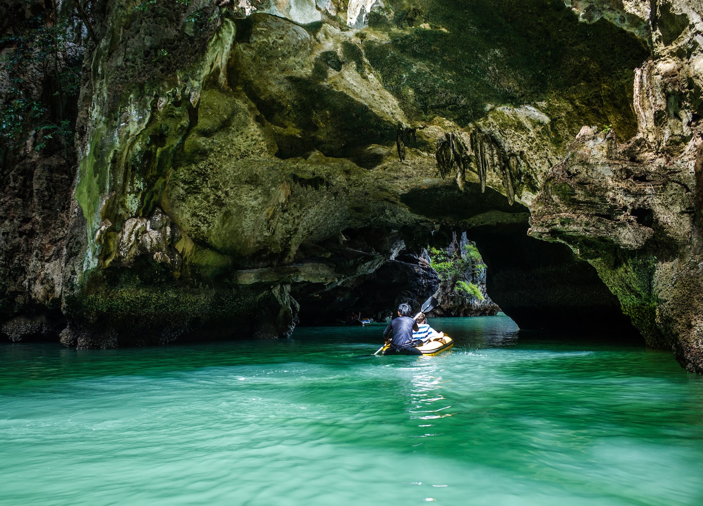 A kayak enters a dim sea cave, framed by limestone walls and calm green water in Phang Nga Bay. - Phuket, Thailand