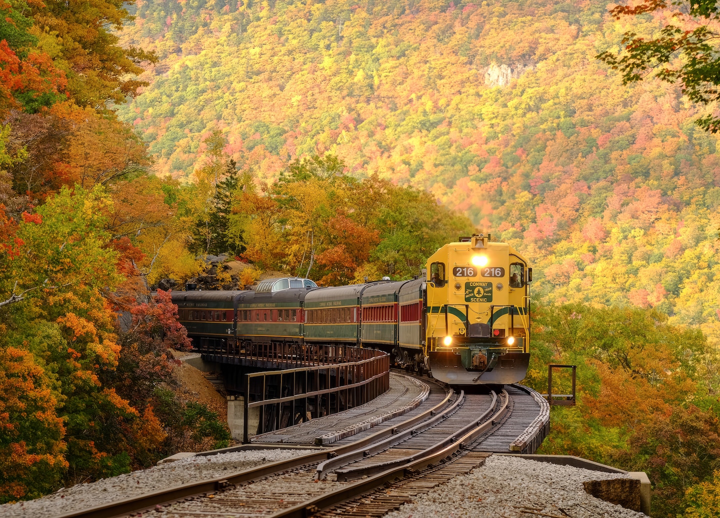 A Conway Scenic Railroad train glides through the White Mountains, surrounded by fall foliage. - Portland, Maine