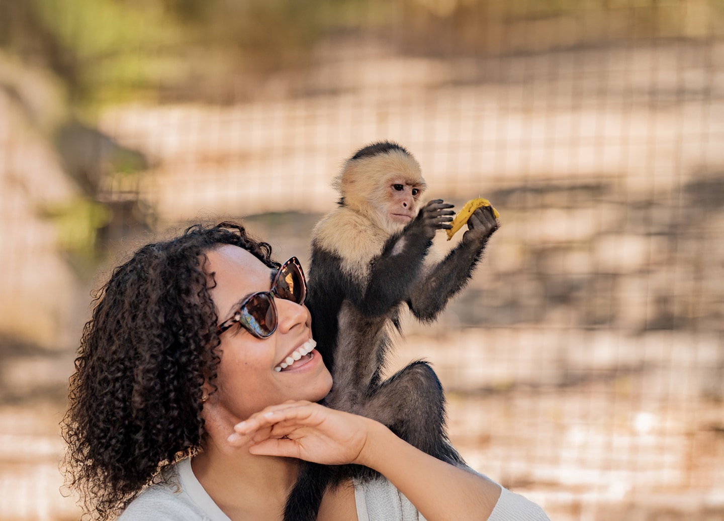 A woman smiles as a small monkey sits on her arm during a Roatán wildlife visit. - Roatan, Honduras