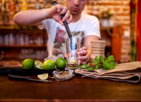 bartender preparing mojito cocktail drink with limes ice and brown sugar
