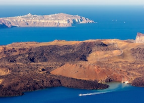 nea kameni volcanic island in santorini greece with little boat leaving the port photographed from