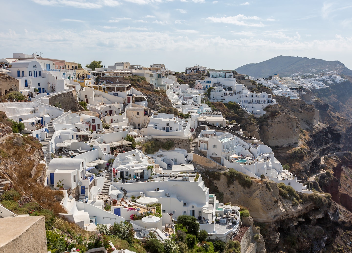 White Oia homes cascade down sunlit cliffs. - Santorini, Greece