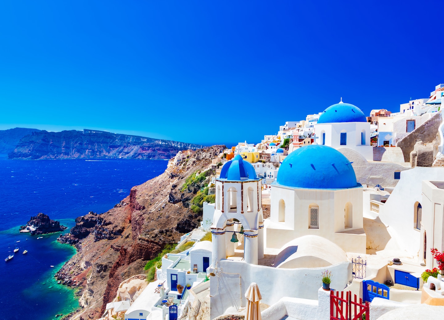 Whitewashed Oia dome overlooks deep blue bay beneath Santorini’s bright sun. - Santorini, Greece